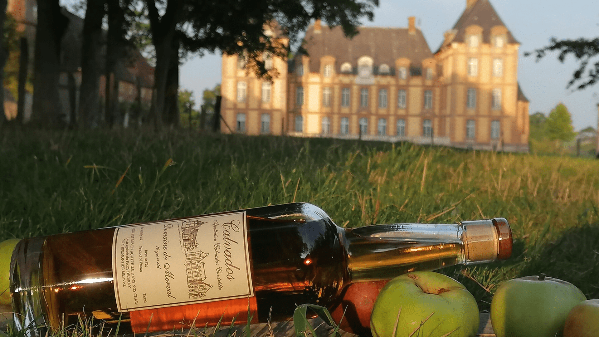 Bouteille de Calvados fabriqué au domaine de Merval et château du domaine en fond.